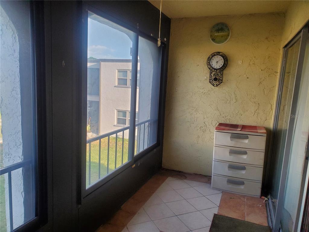 A screened-in balcony features tiled flooring, a plastic storage unit, and a wall-mounted clock — 7701 STARKEY ROAD UNIT 316, SEMINOLE, FL
