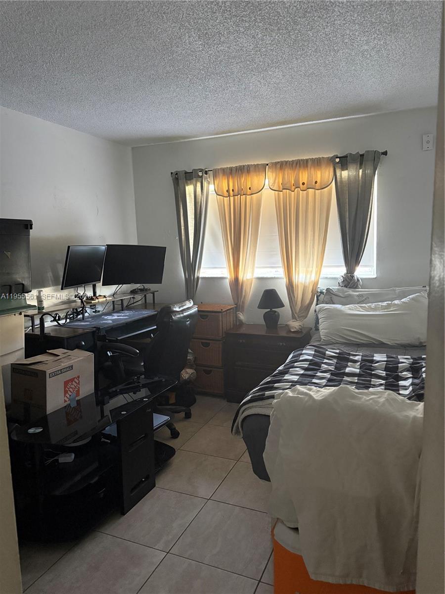 A bedroom features a desk with dual monitors, a bed, and tiled flooring — 7120 NW 179th St # 105, Hialeah FL 33015, HIALEAH, FL