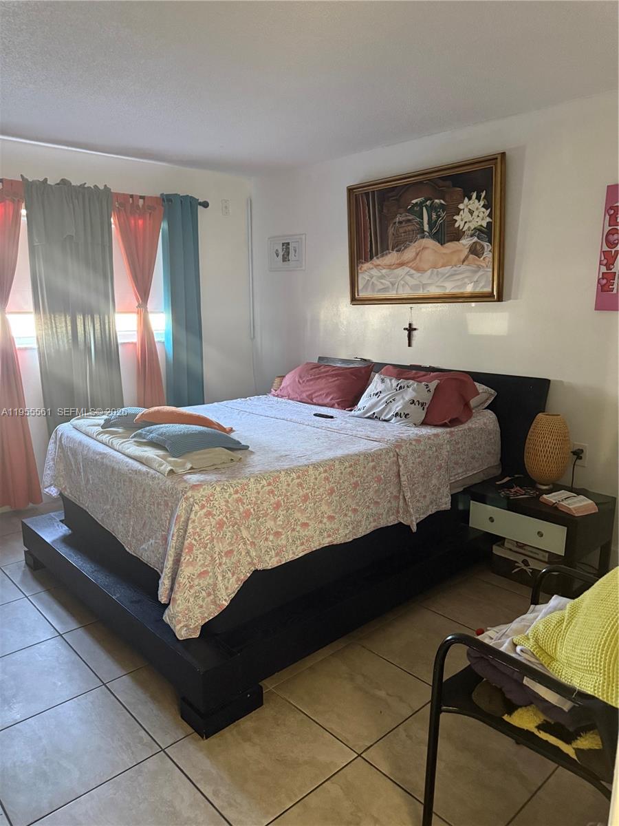 A bedroom features a platform bed with floral bedding, a framed painting, and tiled floors — 7120 NW 179th St # 105, Hialeah FL 33015, HIALEAH, FL