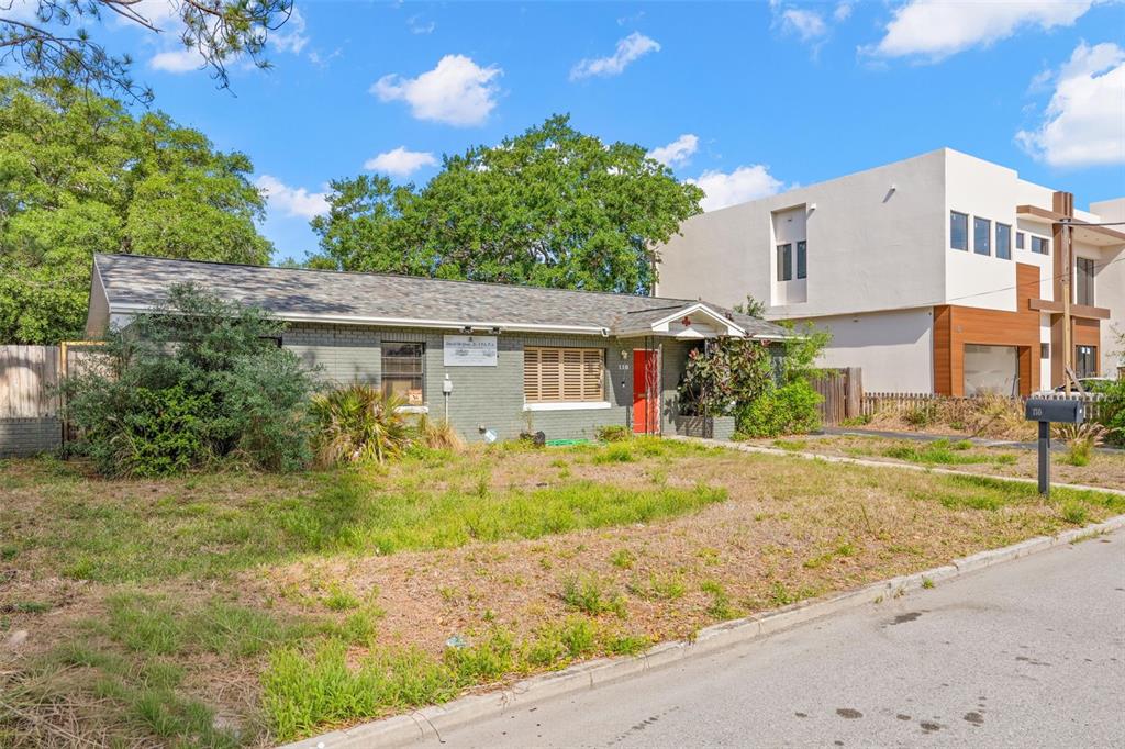 A single-story gray brick house with a red door sits next to a modern building — 110 N LINCOLN AVENUE, TAMPA, FL