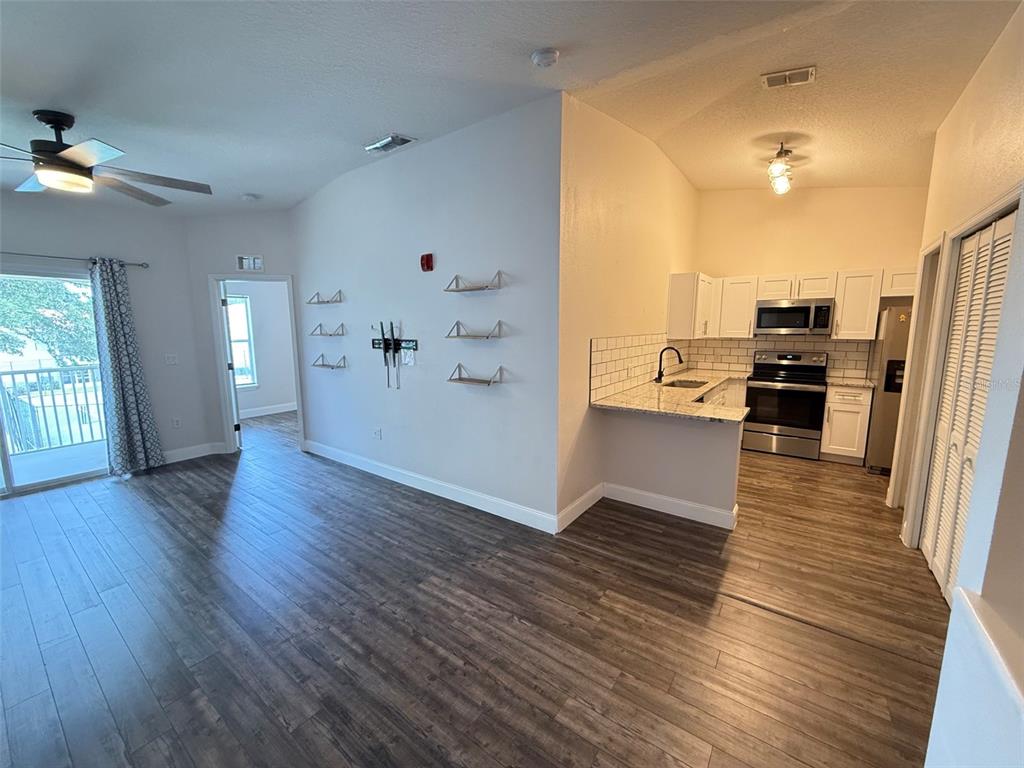 A kitchen with stainless steel appliances and wood-look flooring opens into a living area — 8846 GRAND PALMS CIRCLE UNIT B, KISSIMMEE, FL