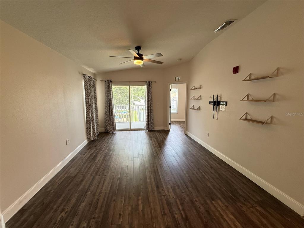 A living room features wood-look flooring, a ceiling fan, sliding glass doors, and wall shelving — 8846 GRAND PALMS CIRCLE UNIT B, KISSIMMEE, FL
