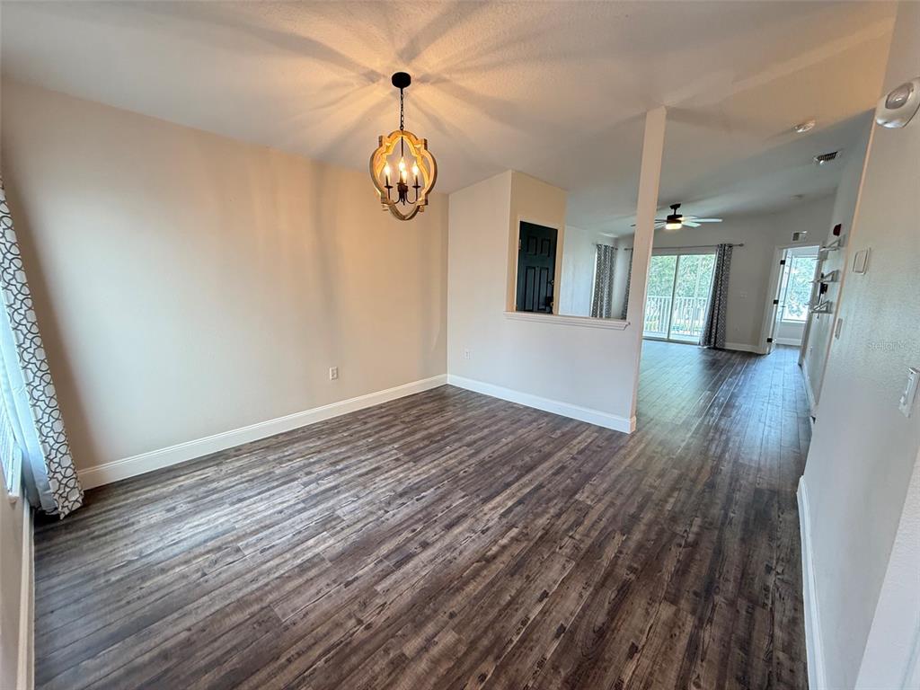 An empty dining room with wood-look flooring, a chandelier, and an adjacent living area — 8846 GRAND PALMS CIRCLE UNIT B, KISSIMMEE, FL