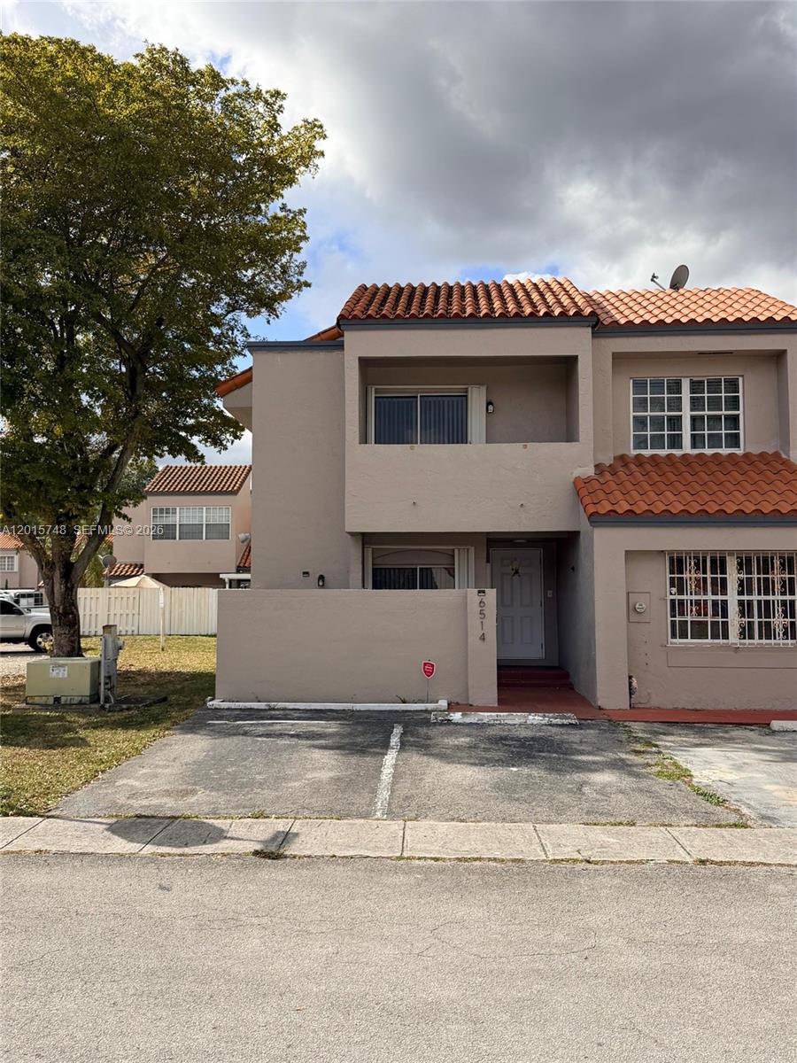 A two-story townhouse with a tan stucco exterior, red tile roof, and private parking space — 6514 SW 128th Pl # 6514, Miami FL 33183, MIAMI, FL