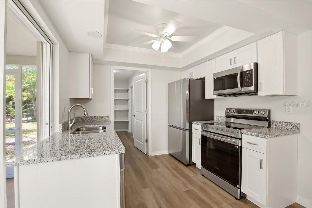 A kitchen with white cabinets, granite countertops, stainless steel appliances, and wood-look flooring — 2278 PINELLAS DRIVE, PUNTA GORDA, FL