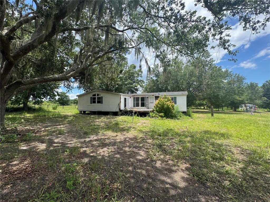 A single-story manufactured home sits on a grassy lot under large, moss-covered oak trees — 38045 COUNTY ROAD 439, EUSTIS, FL