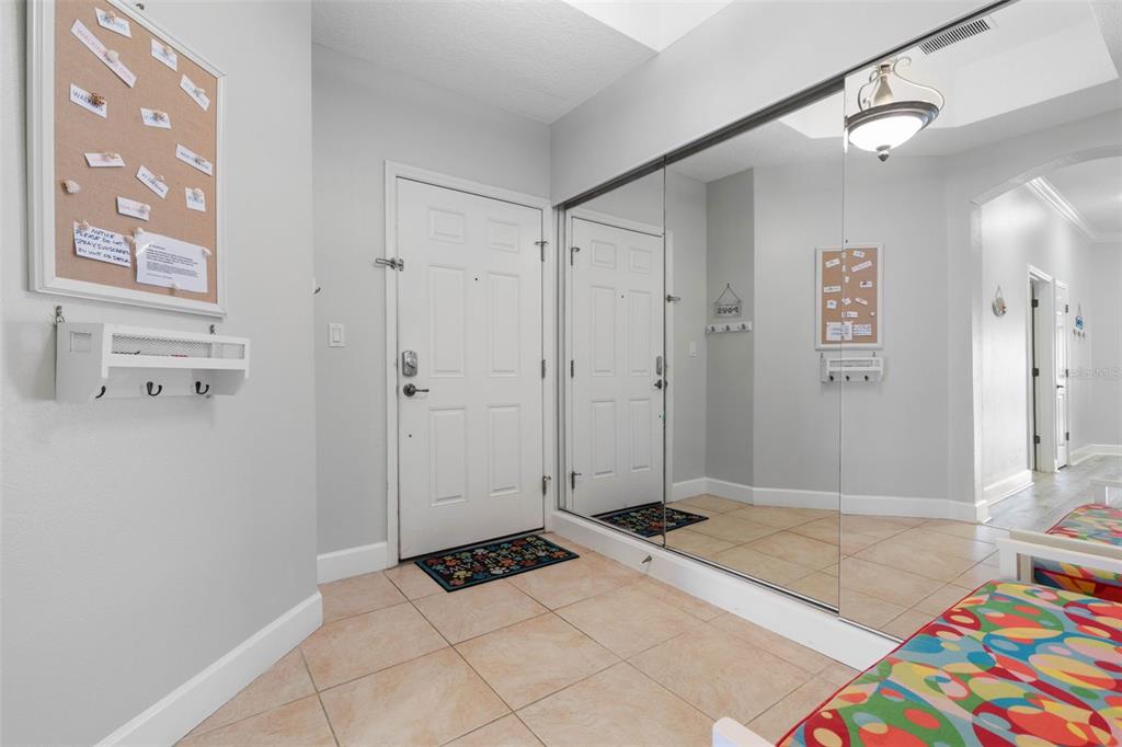 An entryway features a white door, tiled floors, a corkboard, and a large mirrored wall — 800 CINNAMON BEACH WAY UNIT 721, PALM COAST, FL