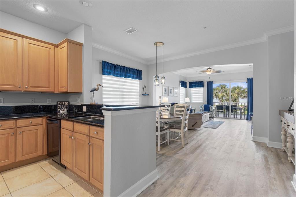 A kitchen with wood cabinets and black countertops opens into a dining and living area — 800 CINNAMON BEACH WAY UNIT 721, PALM COAST, FL