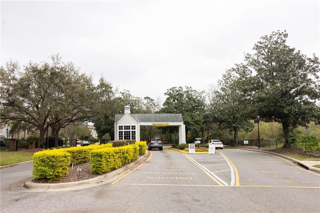 A gated entrance with a guardhouse, paved driveway, and surrounding trees under an overcast sky — 5005 CITY STREET UNIT 1317, ORLANDO, FL