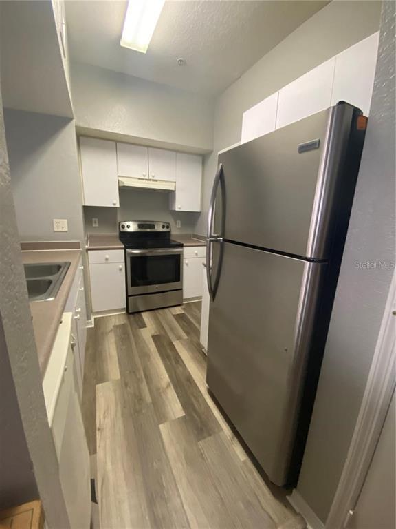 A galley kitchen features stainless steel appliances, white cabinets, and wood-look flooring — 5005 CITY STREET UNIT 1317, ORLANDO, FL