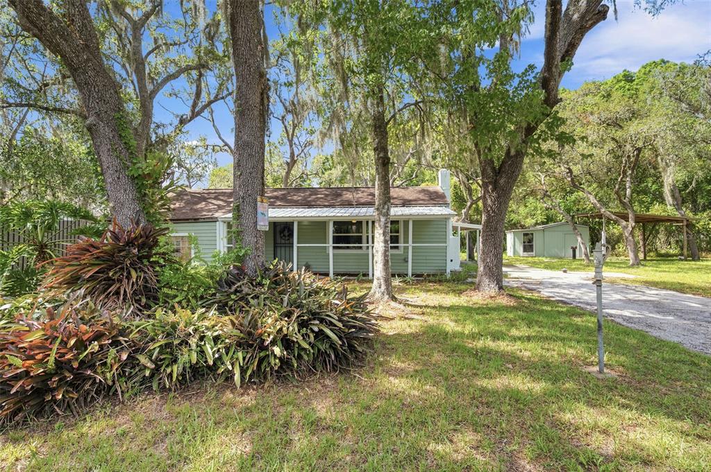 A light green house with a front porch sits among large trees on a grassy lot — 12307 EAGLE LAKE AVENUE, NEW PORT RICHEY, FL