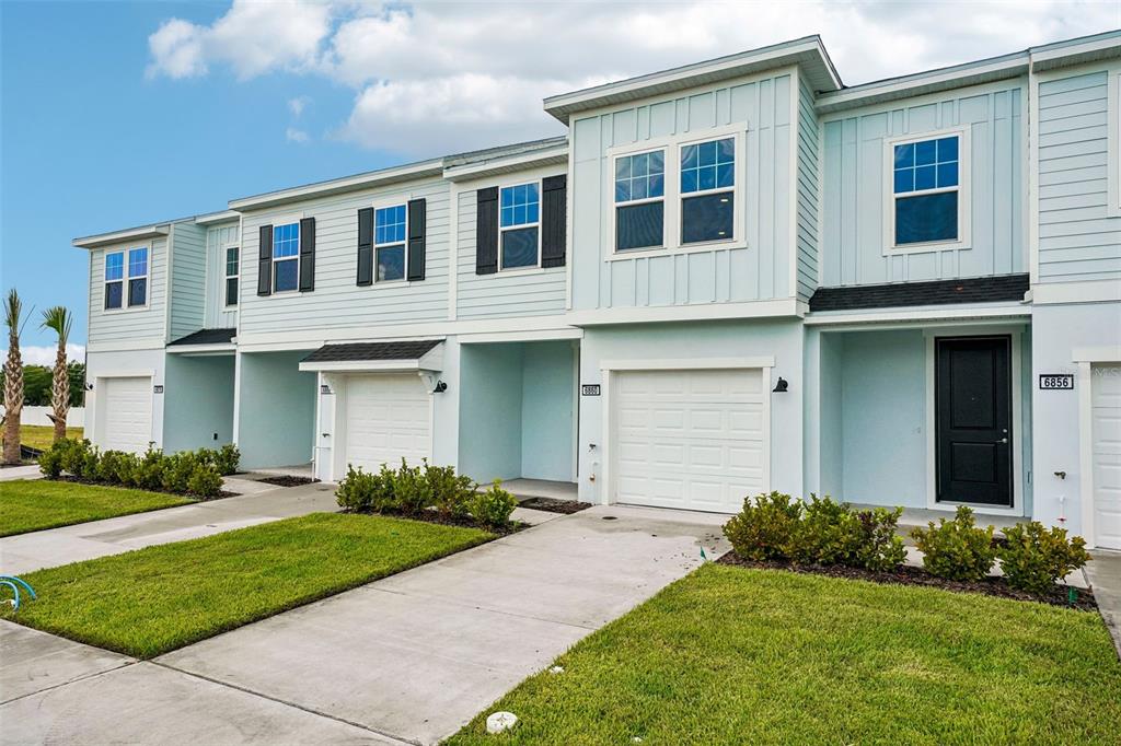 A light blue exterior wall features a black front door and a white garage door — 6860 HOLCOMBE DOWN DRIVE, ZEPHYRHILLS, FL