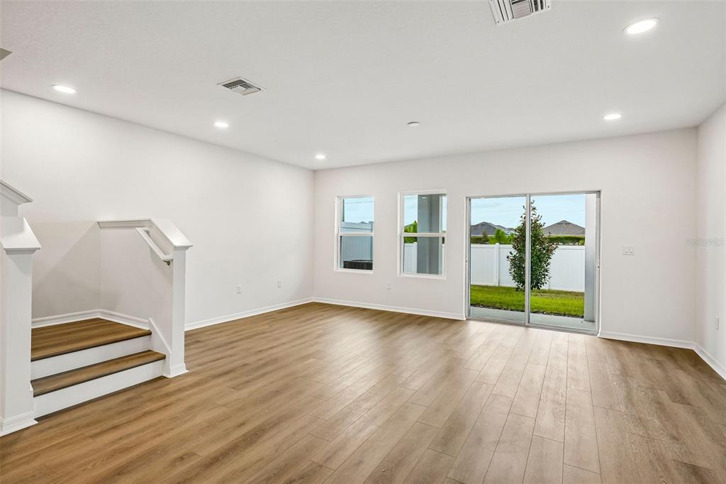 An empty living room with light wood-look flooring, white walls, recessed lighting, and sliding doors — 6860 HOLCOMBE DOWN DRIVE, ZEPHYRHILLS, FL