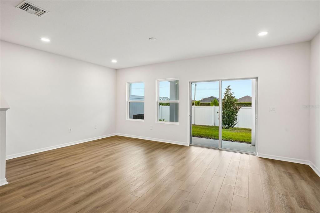 A living room features light wood flooring, a gray sofa, two armchairs, and sliding glass doors — 6860 HOLCOMBE DOWN DRIVE, ZEPHYRHILLS, FL