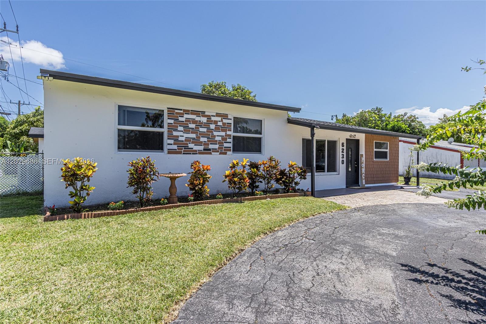 A single-story house with a white stucco facade, decorative stone accents, and a paved driveway — 6230 SW 16th Ct, North Lauderdale FL 33068, NORTH LAUDERDALE, FL