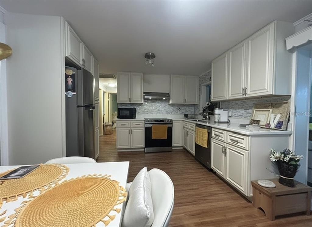A kitchen features white cabinetry, stainless steel appliances, a tiled backsplash, and wood-look flooring — 2455 ROYAL ROAD, DELAND, FL