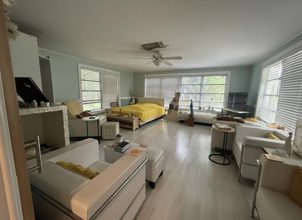 A spacious room features light wood flooring, a yellow bed, and white modern seating furniture — 2455 ROYAL ROAD, DELAND, FL