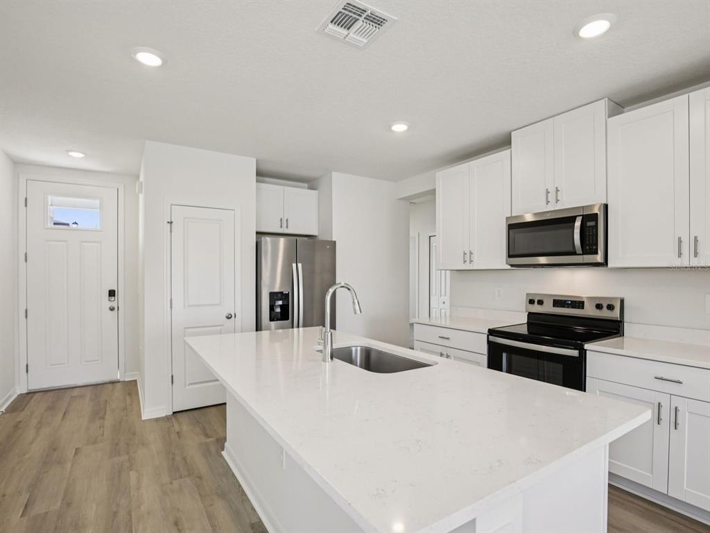 A modern kitchen features white cabinets, stainless steel appliances, and a large quartz-topped island — 11255 BELLEWOOD TERRACE, PARRISH, FL