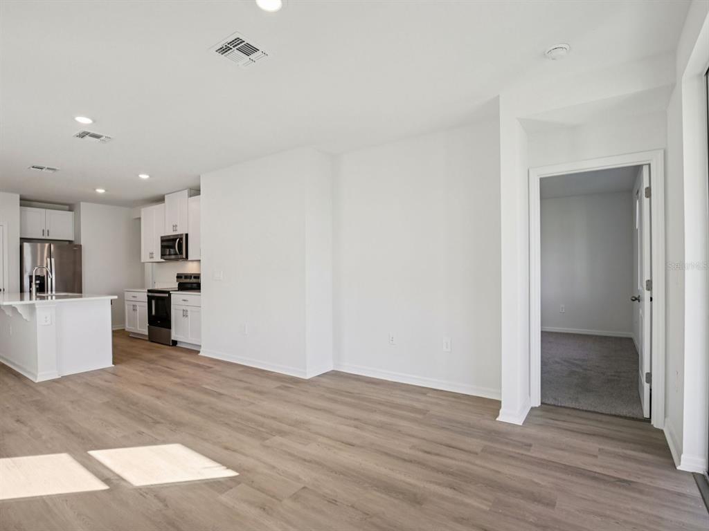 An open-concept living area features light wood-look flooring, white walls, and an adjacent modern kitchen — 11255 BELLEWOOD TERRACE, PARRISH, FL