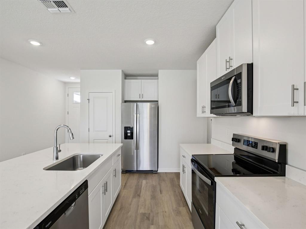 A modern kitchen features white cabinets, stainless steel appliances, and a large quartz-topped island — 11255 BELLEWOOD TERRACE, PARRISH, FL