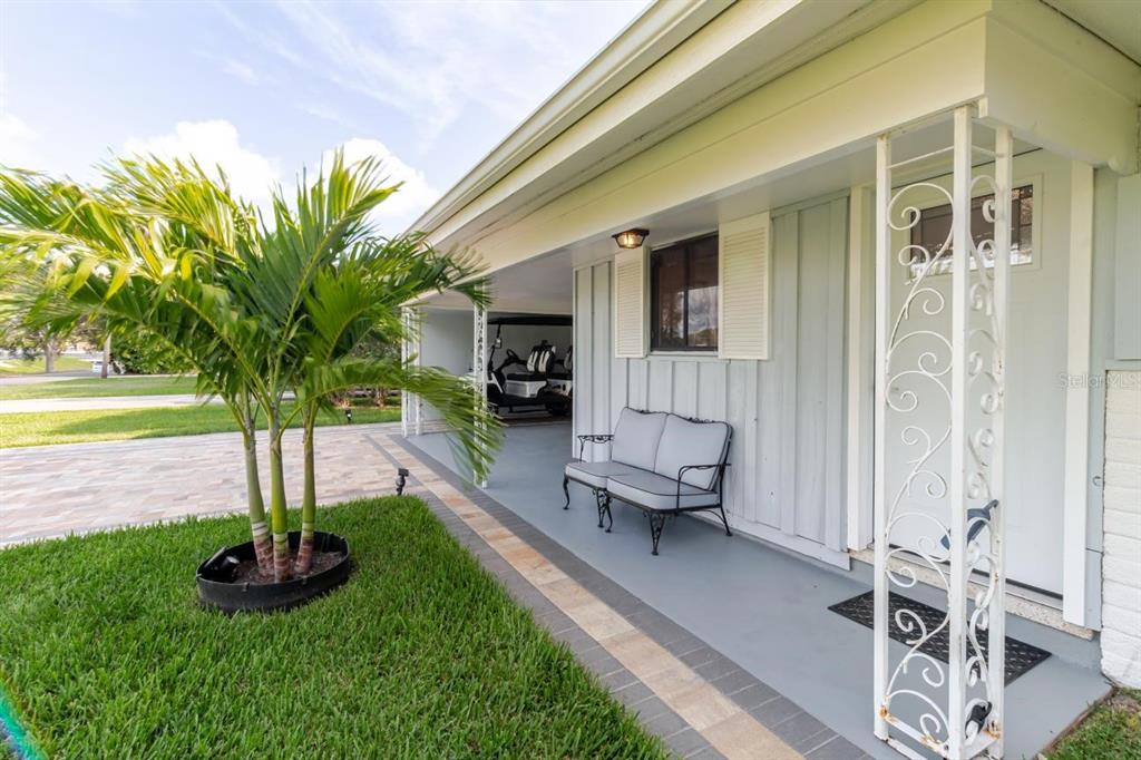A covered porch features a gray bench, decorative metal columns, and a view of a carport — 96 NEW YORK AVENUE, DUNEDIN, FL