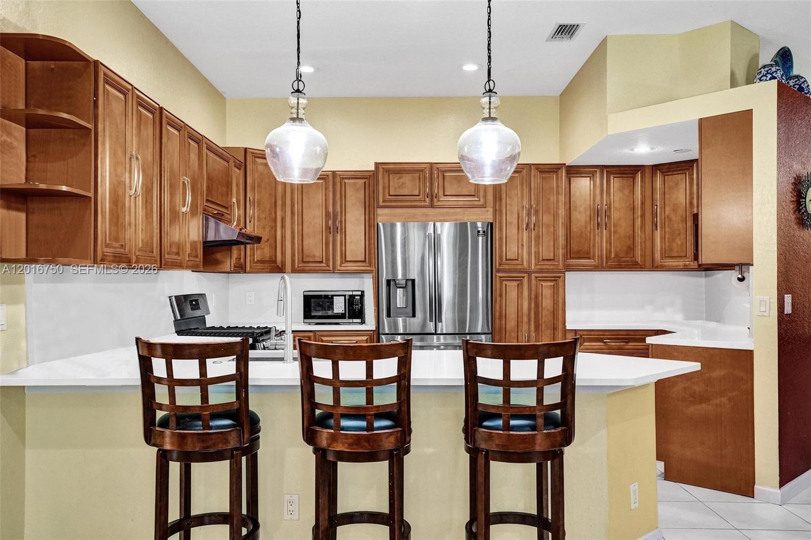 A kitchen features wood cabinets, stainless steel appliances, and a breakfast bar with three chairs — 4401 SW 74th Ter, Davie FL 33314, DAVIE, FL