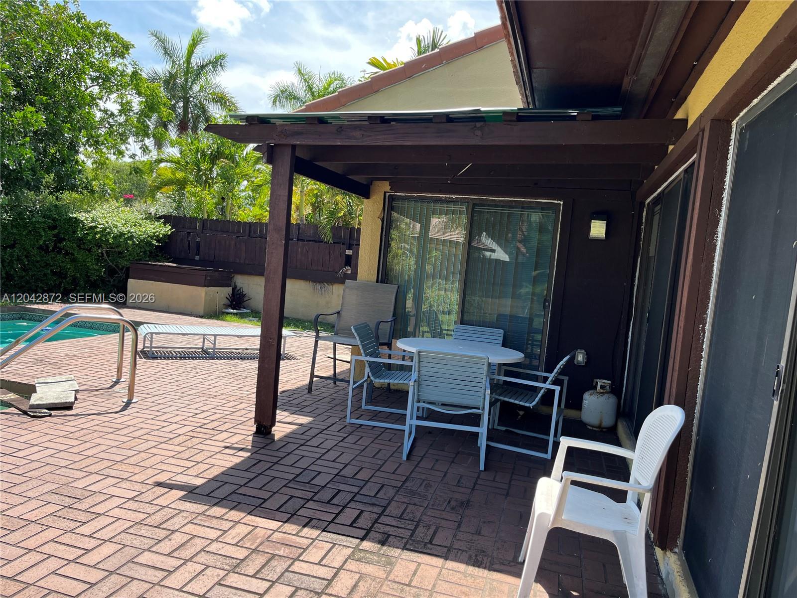 A patio with a wooden pergola, dining set, and pool access overlooks a backyard — 1020 NE 202nd Ter, Miami FL 33179, MIAMI, FL