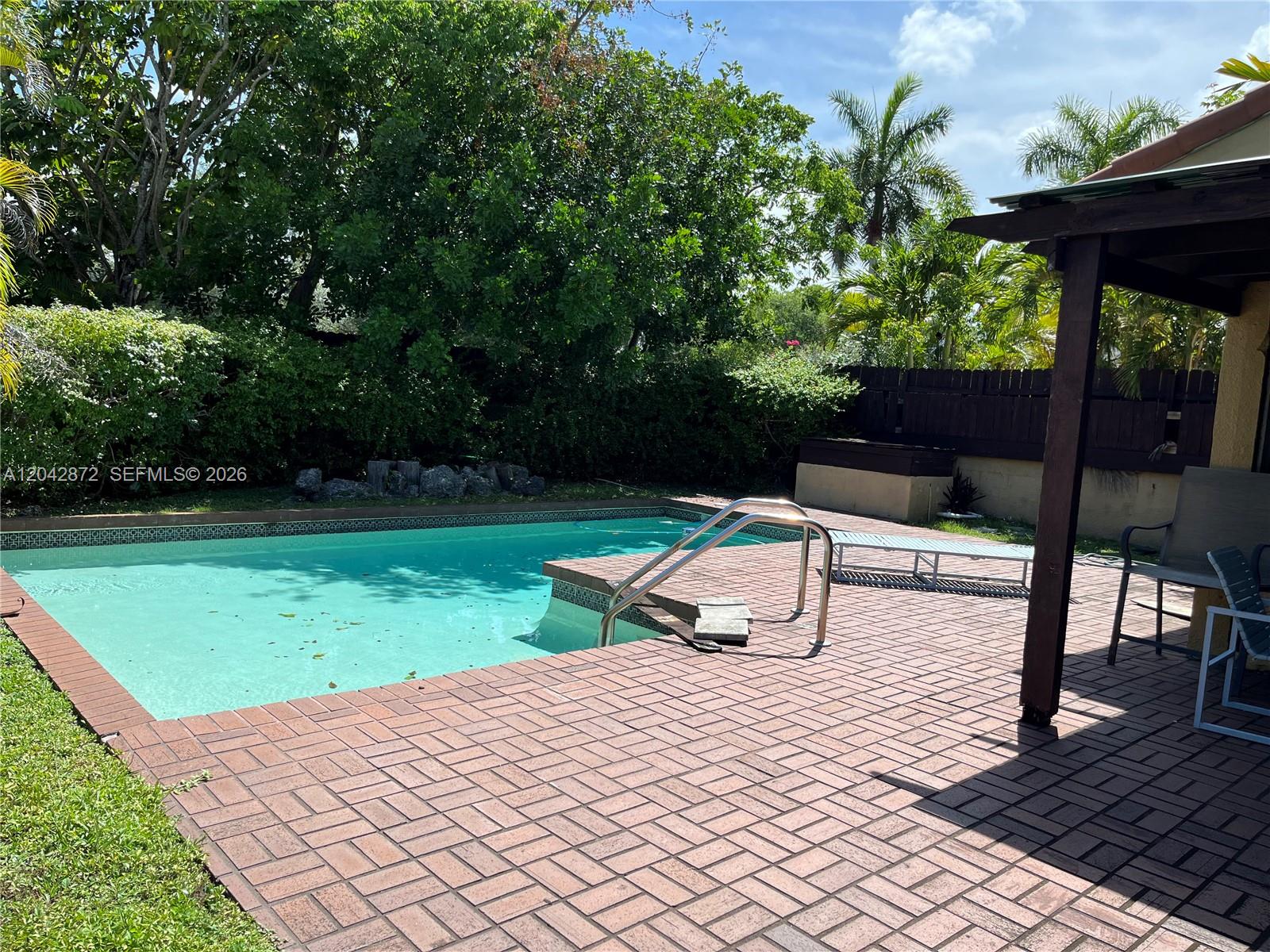 A backyard features a rectangular swimming pool with a brick paver deck and patio cover — 1020 NE 202nd Ter, Miami FL 33179, MIAMI, FL