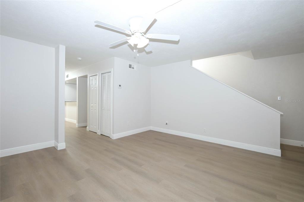 An interior view of a living area with light wood flooring, white walls, and stairs — 4029 HENLEY ROAD UNIT 1705, ORLANDO, FL