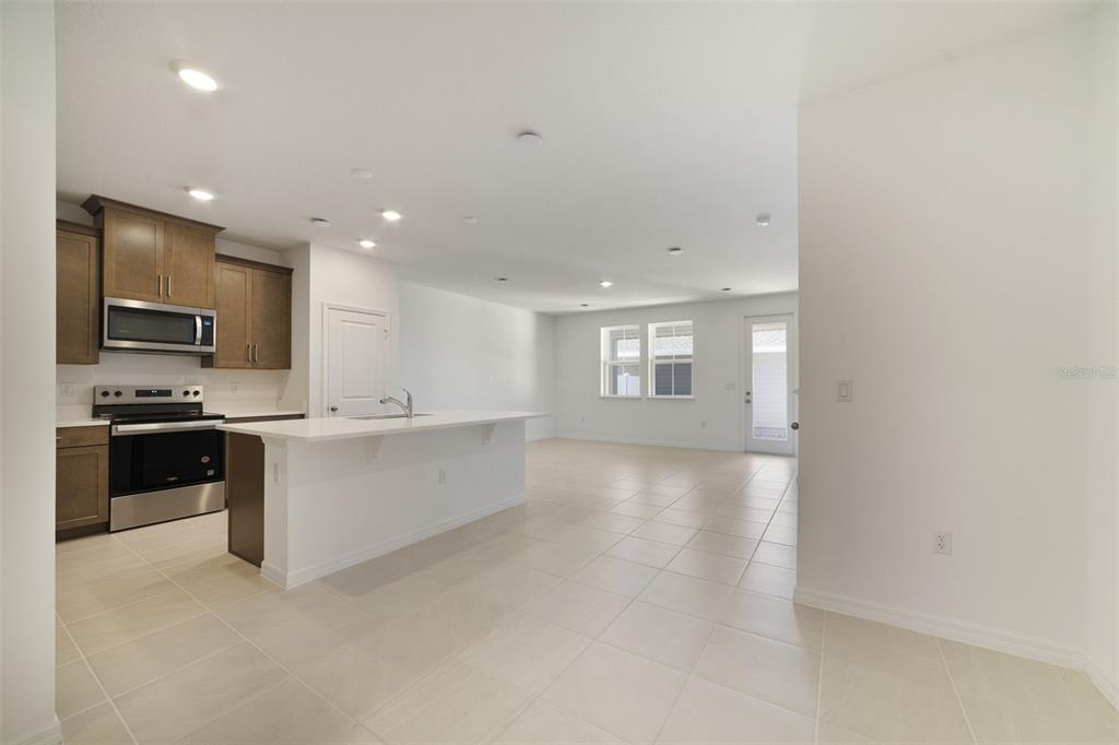 A kitchen with stainless steel appliances and a white island opens into a living area — 688 LOLA LANE, OVIEDO, FL