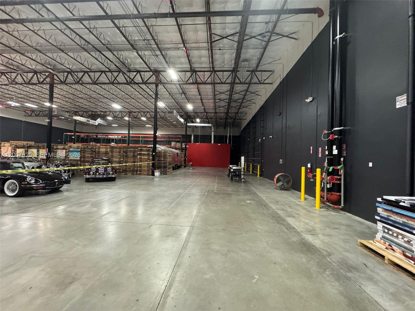 A spacious warehouse interior features concrete floors, exposed ceiling trusses, and a black accent wall — 3450 NW 115th Ave, Doral FL 33178, DORAL, FL
