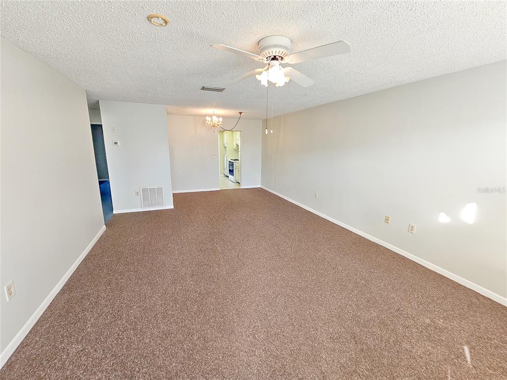 A spacious, carpeted living room features a ceiling fan and an open doorway to a kitchen — 3128 59TH STREET S UNIT 204, GULFPORT, FL