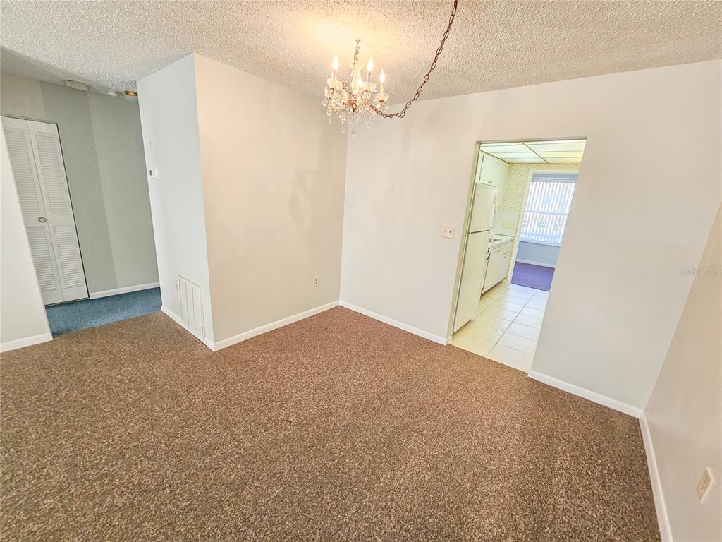 A dining area with brown carpet, a crystal chandelier, and a doorway leading to a kitchen — 3128 59TH STREET S UNIT 204, GULFPORT, FL