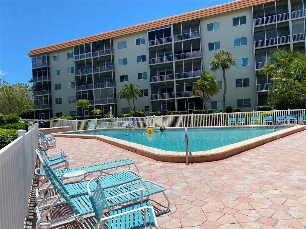 A multi-story apartment building overlooks a swimming pool with lounge chairs on a patio — 1600 1ST AVENUE W UNIT 206A, BRADENTON, FL