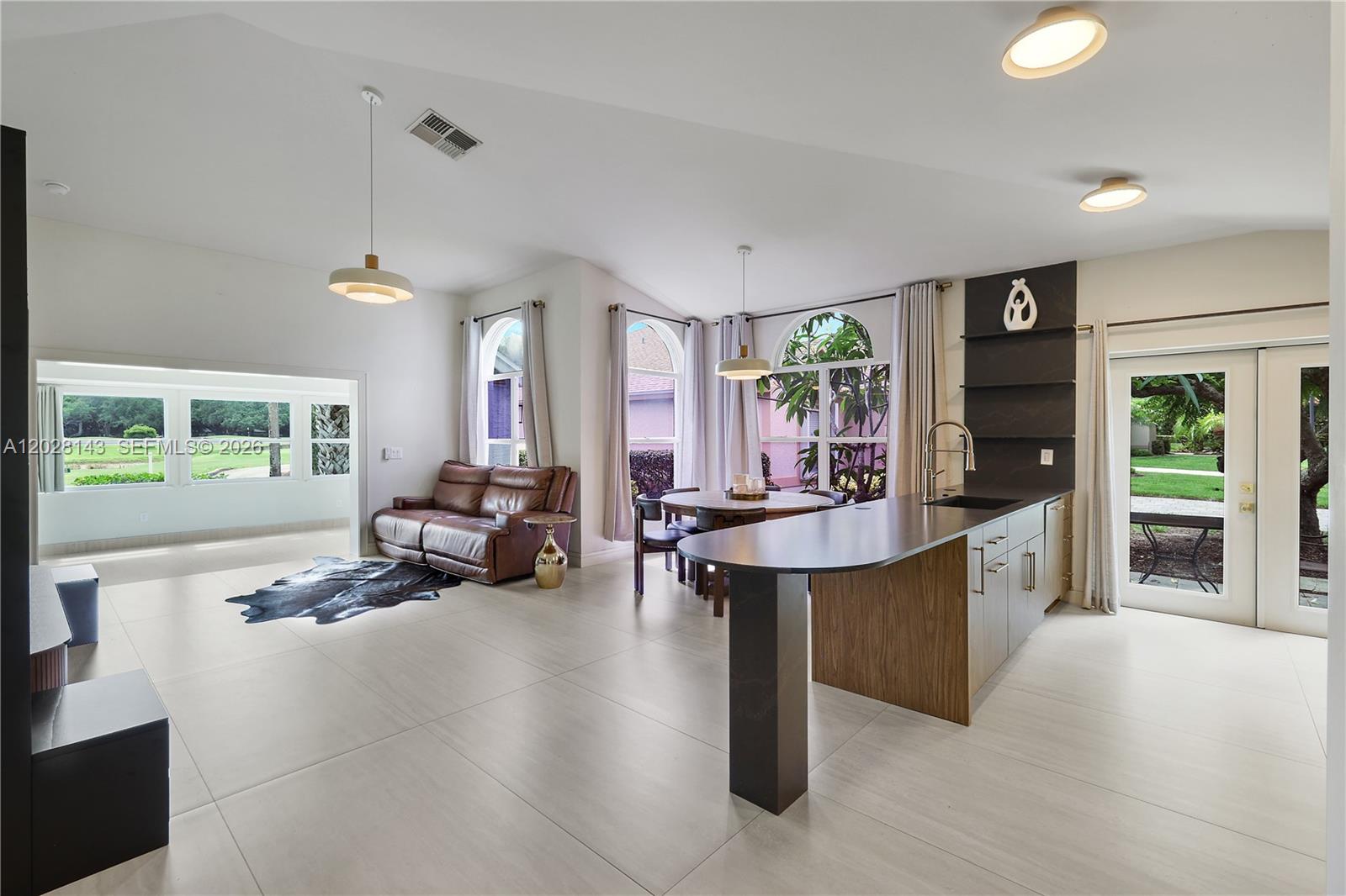 A modern open-concept kitchen and living area features tile floors, a kitchen island, and windows — 21167 Butchers Holler, Estero FL 33928, ESTERO, FL
