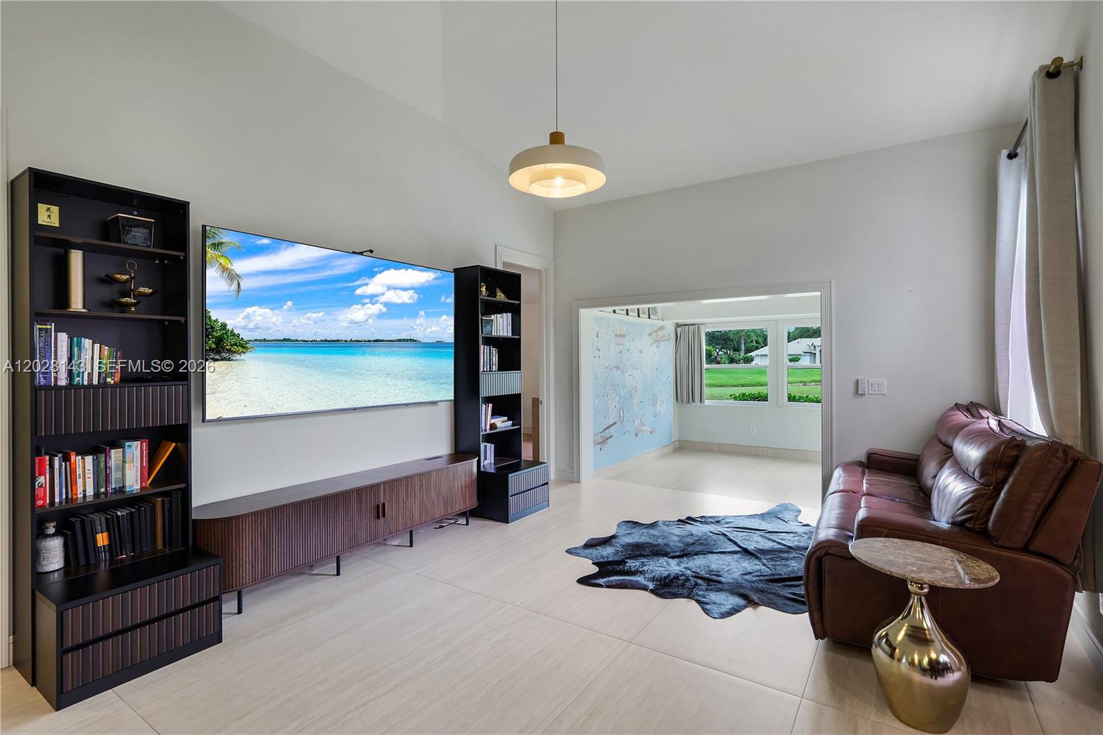 A living room features a large wall-mounted television, dark shelving, and a brown leather sofa — 21167 Butchers Holler, Estero FL 33928, ESTERO, FL