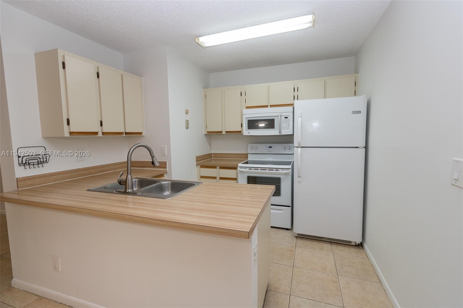 A kitchen features light wood-look countertops, white cabinets, white appliances, and beige tile flooring — 18328 NW 68th Ave # P, Hialeah FL 33015, HIALEAH, FL