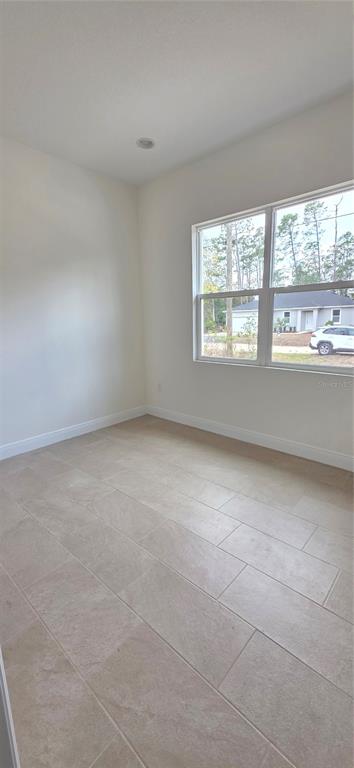 An empty room with light-colored tile flooring, white walls, and a window overlooking a neighborhood — 1569 9TH AVENUE, DELAND, FL