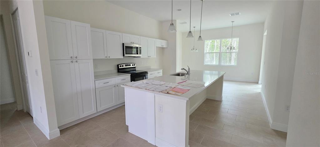A white kitchen features a center island, stainless steel appliances, and light-colored tile flooring — 1569 9TH AVENUE, DELAND, FL