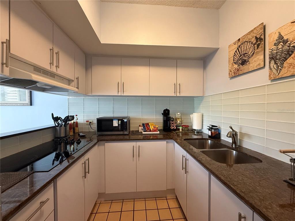 A galley kitchen features white cabinets, dark granite countertops, a double sink, and tiled flooring — DR BEACH VILLAGE UNIT 119, HUMACAO, PR