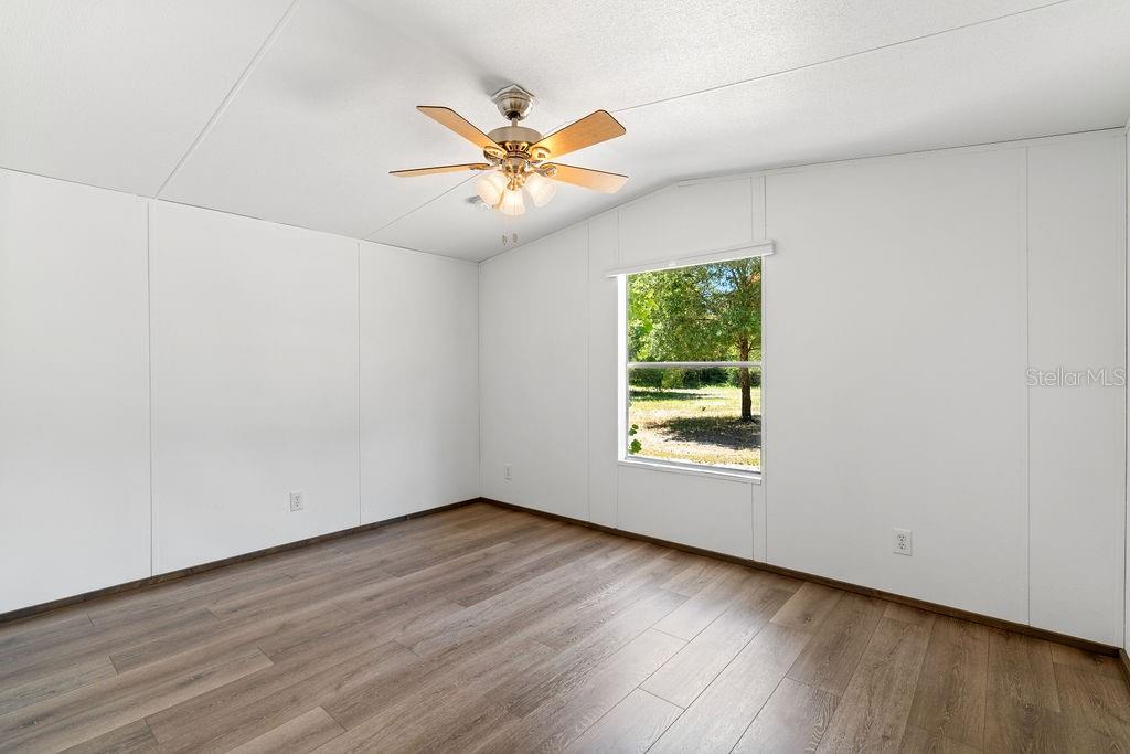 An empty room with white walls, wood-look flooring, a ceiling fan, and a single window — 27133 MILLER ROAD, DADE CITY, FL