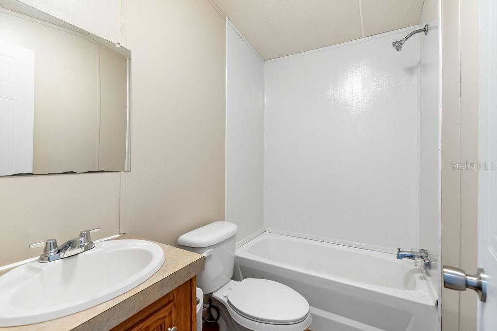 A bathroom features a white bathtub with a shower, a toilet, and a wooden vanity — 27133 MILLER ROAD, DADE CITY, FL