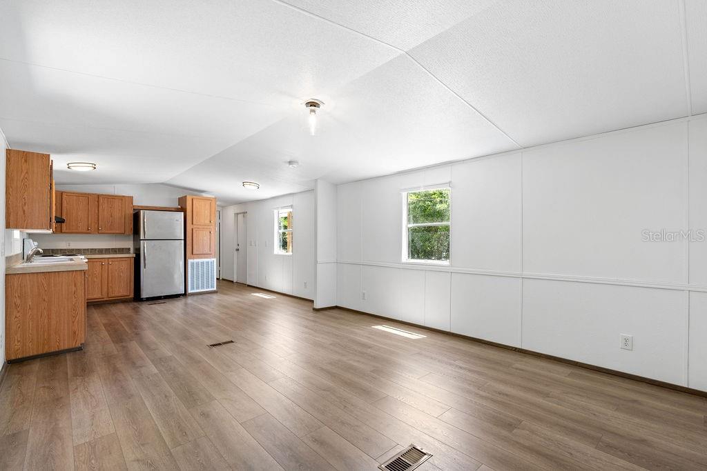 An open-concept kitchen and living area features light wood-look flooring and white paneled walls — 27133 MILLER ROAD, DADE CITY, FL
