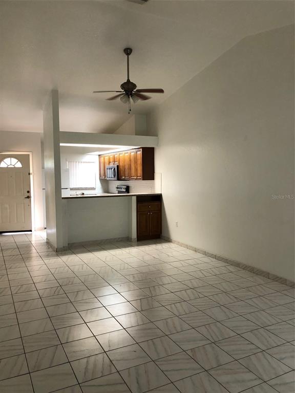 An open-concept living area features white tile flooring, a ceiling fan, and a wood-cabinet kitchen — 25385 SANDHILL BOULEVARD UNIT D2, PUNTA GORDA, FL