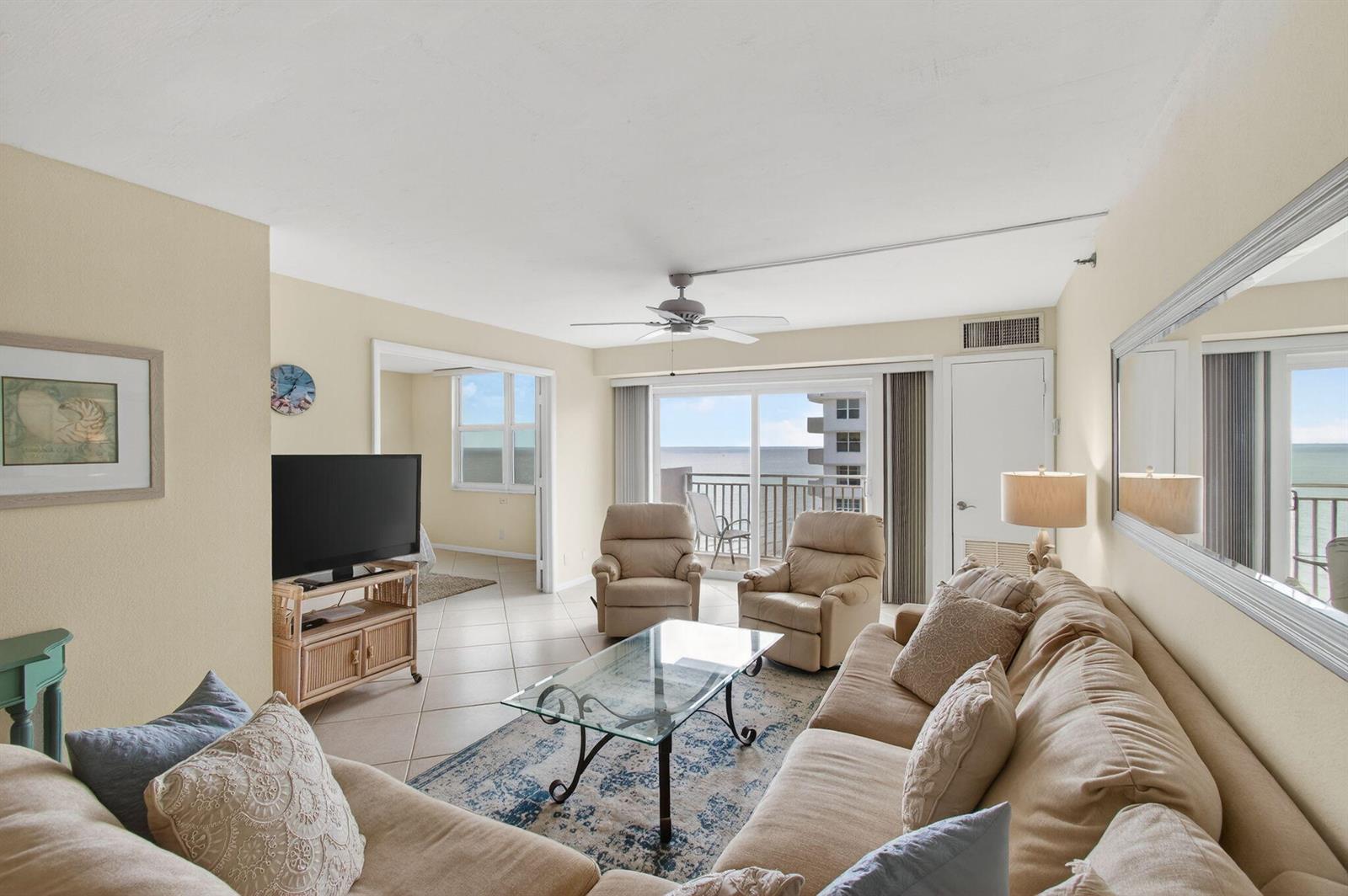 A living room features beige furniture, a glass coffee table, and a balcony overlooking water — 4505 S Ocean Boulevard # 905, Highland Beach FL 33487, HIGHLAND BEACH, FL