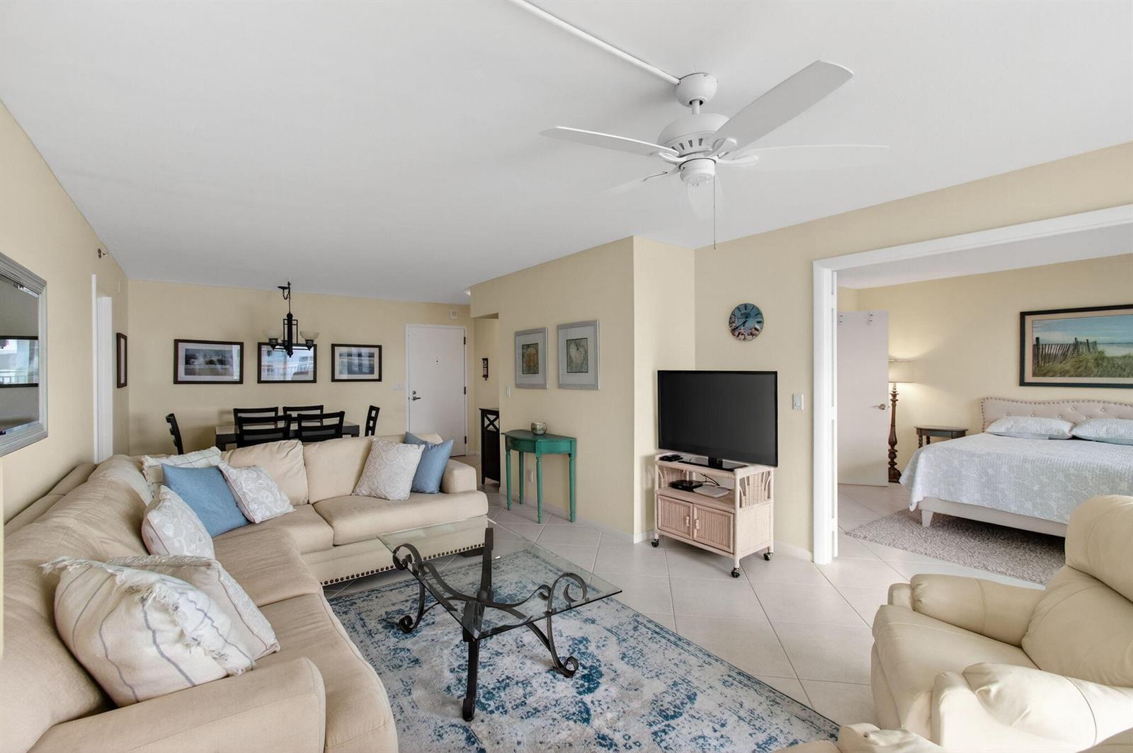 A living room with a beige sectional, glass coffee table, and an adjacent bedroom — 4505 S Ocean Boulevard # 905, Highland Beach FL 33487, HIGHLAND BEACH, FL
