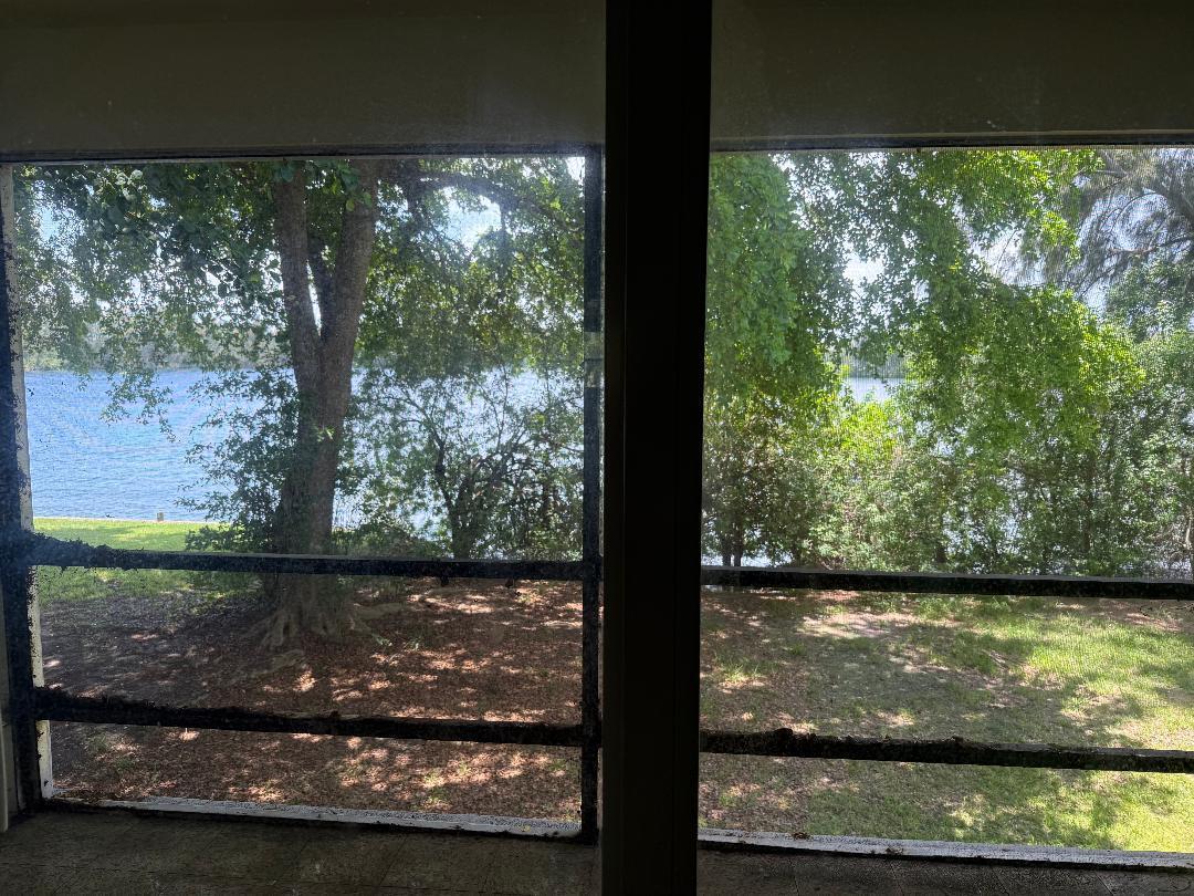 A view of a lake and trees through a screened-in porch with dark metal framing — 3941 Crystal Lake Drive, Pompano Beach FL 33064, POMPANO BEACH, FL