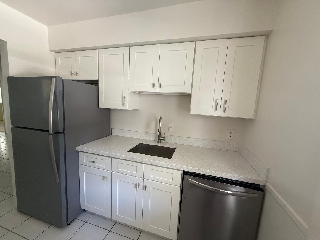 A small kitchen features white shaker cabinets, stainless steel appliances, and light-colored speckled countertops — 3941 Crystal Lake Drive, Pompano Beach FL 33064, POMPANO BEACH, FL