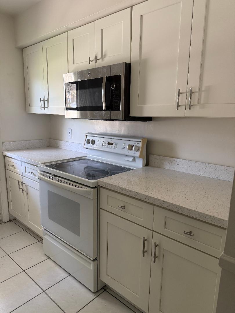 A kitchen features white shaker cabinets, speckled countertops, a white stove, and a stainless microwave — 3941 Crystal Lake Drive, Pompano Beach FL 33064, POMPANO BEACH, FL