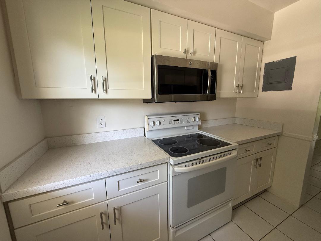 A kitchen features white cabinets, a stainless steel microwave, a white stove, and speckled countertops — 3941 Crystal Lake Drive, Pompano Beach FL 33064, POMPANO BEACH, FL